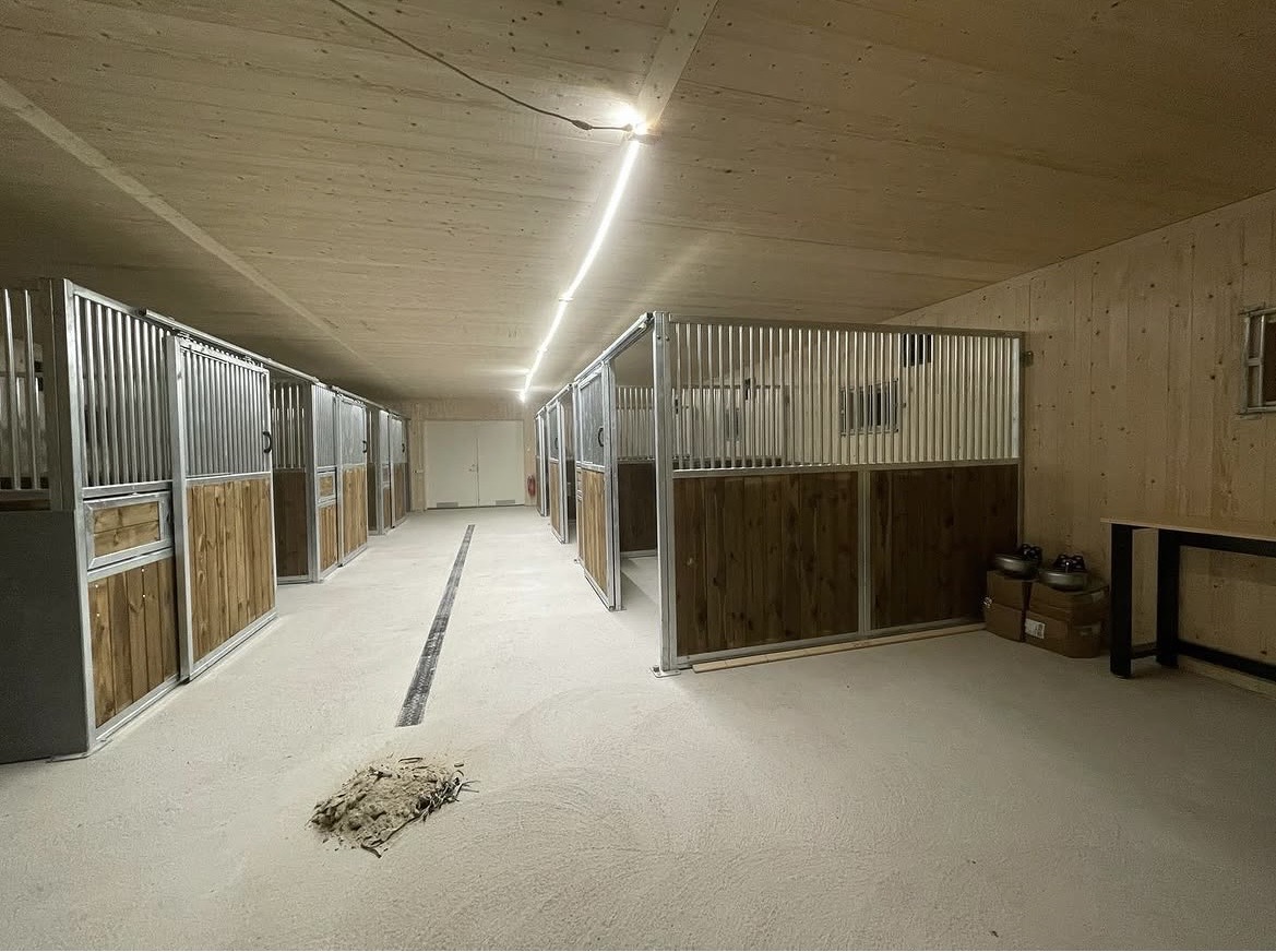 Nybyggt stall med boxar i trä och stål, LED-belysning